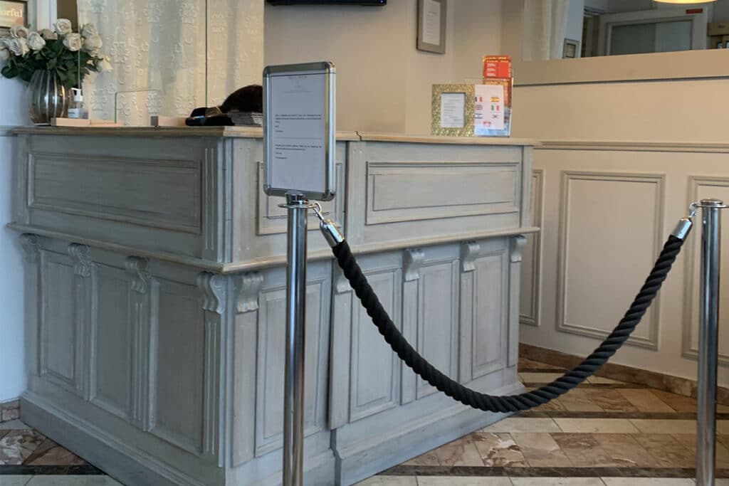 Réception d'Hôtel de Style Vintage avec Comptoir Gris Comptoir de réception d'hôtel vintage en bois gris avec bouquet de roses blanches et poteaux de guidage à corde noire.