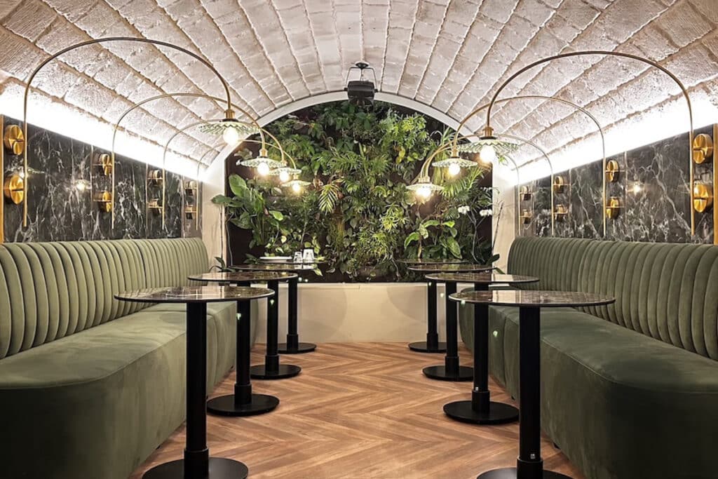 Restaurant de Luxe : Banquettes Velours et Mur Végétal Restaurant chic avec banquettes en velours vert, mur végétal et plafond voûté sous des arcs lumineux dorés.