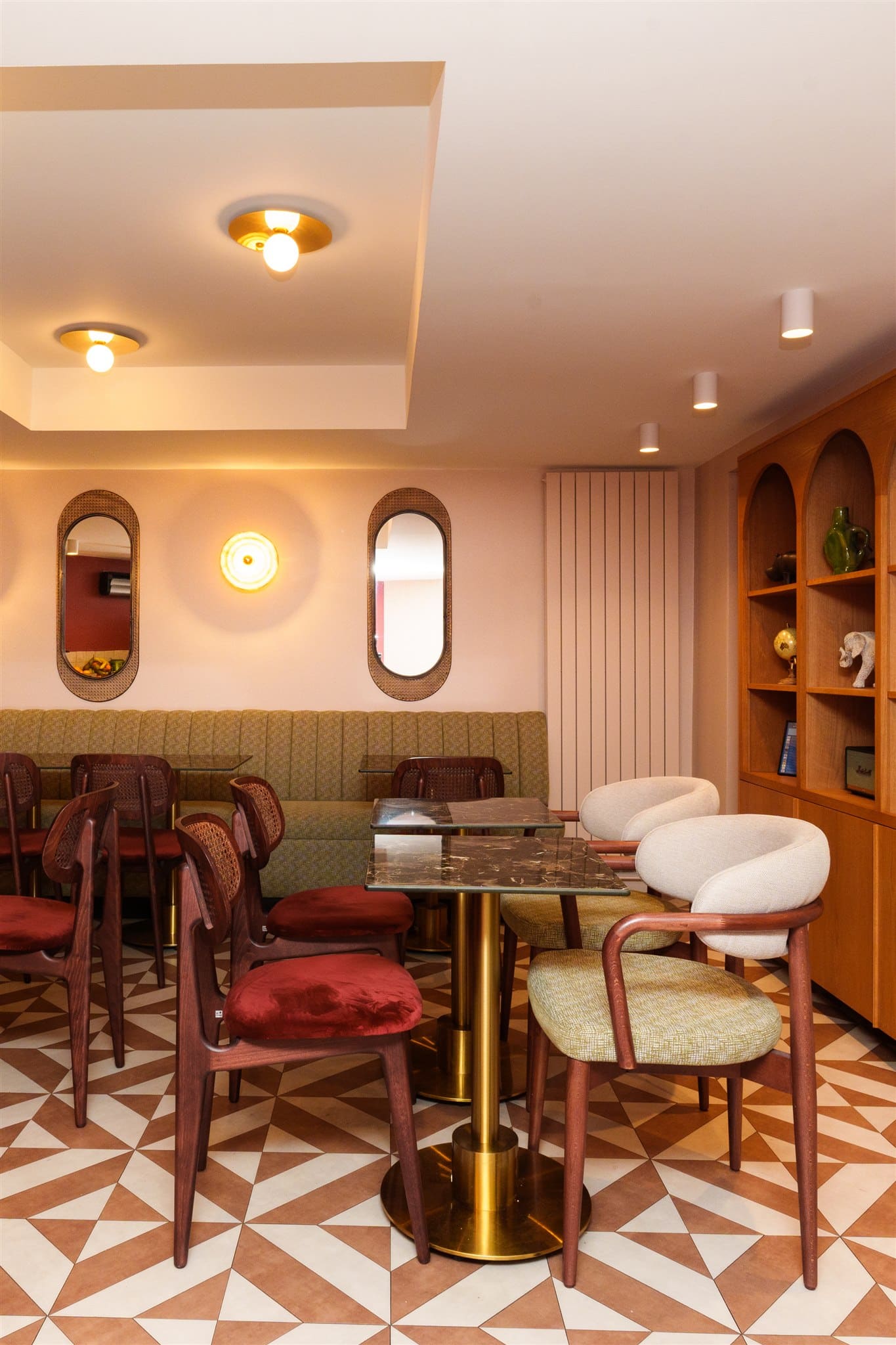 Design intérieur rétro chic d'un café. Banquette olive, miroirs ovales en rotin, sol géométrique terracotta, étagères en bois clair.