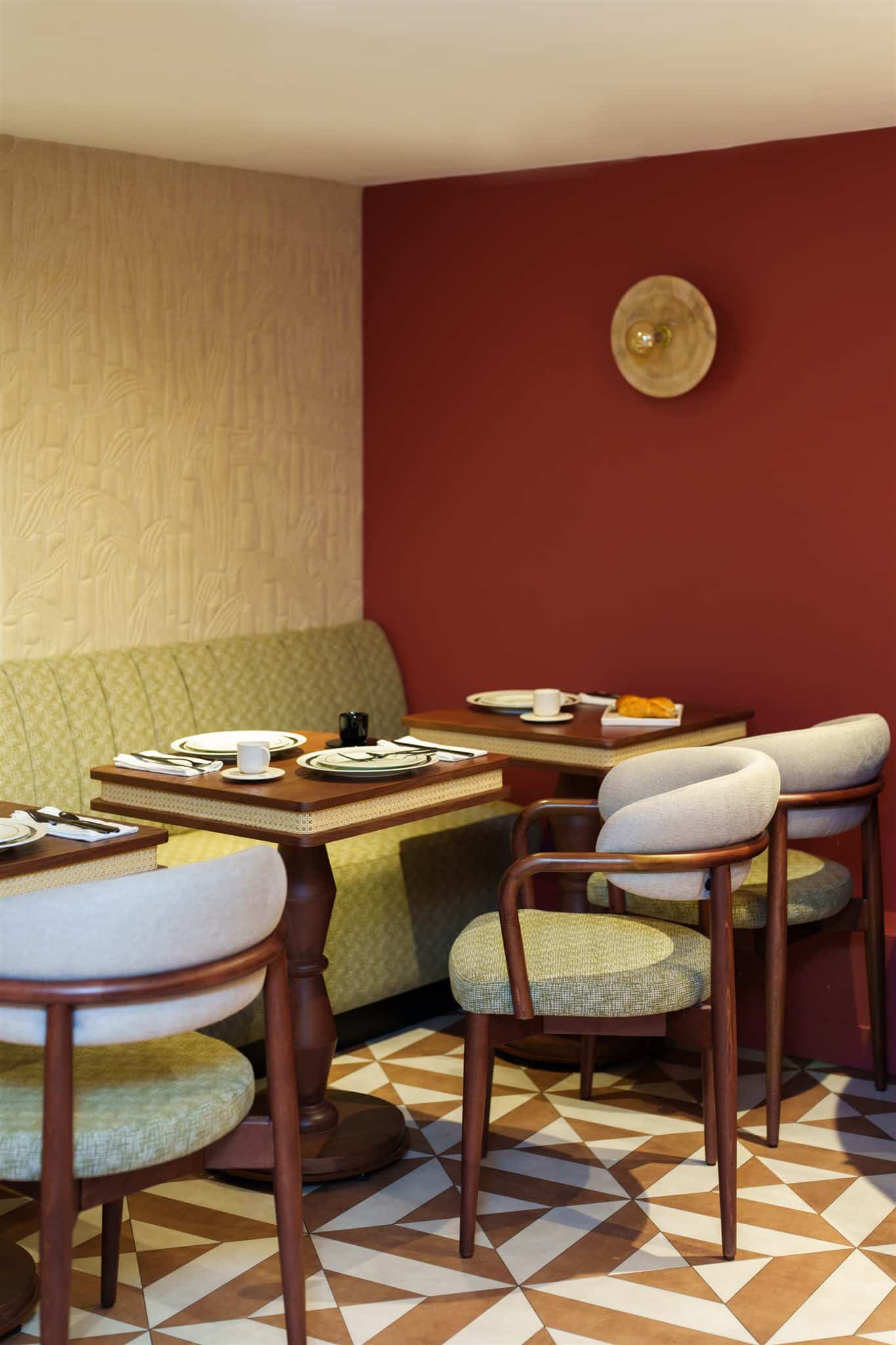 Intérieur de restaurant coloré : banquette verte, mur rouge bordeaux, papier peint bambou. Chaises bois, tables canne, sol géométrique brun.